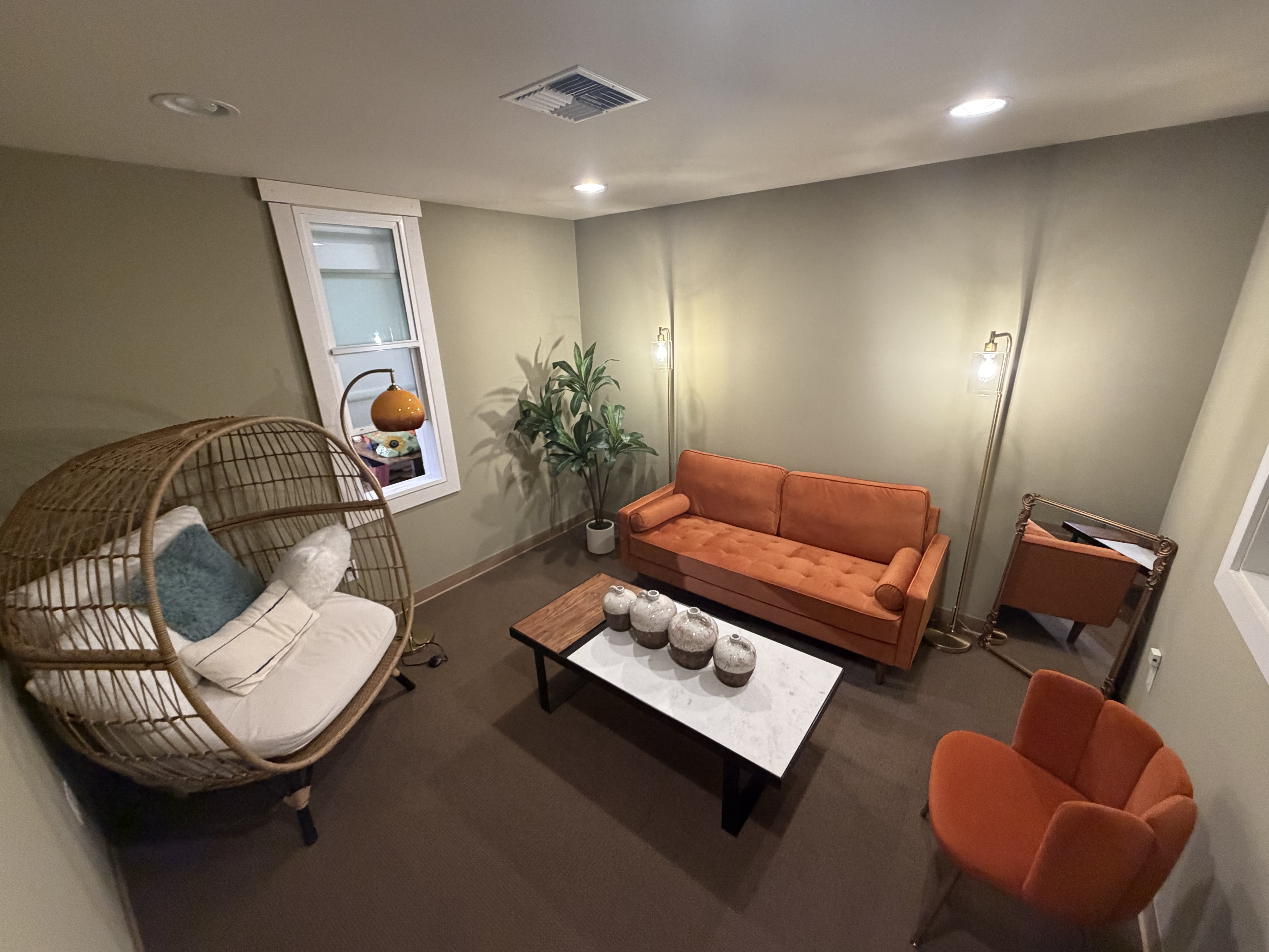 Closer angle of the hanging wicker chair and orange sofa in the creative studio